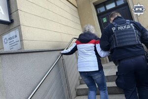 na zdjęciu policjant prowadzący kobietę do budynku komendy
