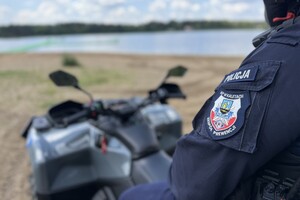 na zdjęciu fragment policjanta, który siedzi na quadzie, na plaży przy akwenie