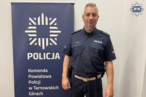 na zdjęciu aspirant Jakubowski przy banerze z napisem policja