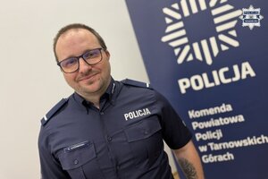 na zdjęciu posterunkowy Godzimirski, a za nim baner z napisem policja