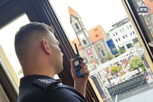 na zdjęciu policjant z radiotelefonem w ręku, wyglądający przez okno