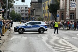 na zdjęciu radiowóz w poprzek jezdni, obok policjant i widownia
