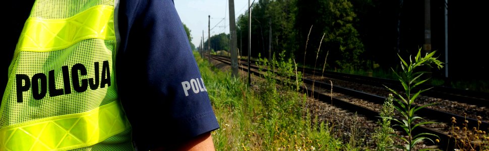 Na zdjęciu widoczna żółta kamizelka z napisem "POLICJA", a w tle tory kolejowe.