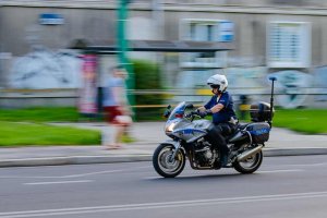 Na zdjęciu widoczny policjant na motorze, który jedzie po drodze