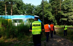 Policjant oraz funkcjonariusze SOK i pracownicy polskich linii kolejowych idą w stronę torów, w tle widać pędzący pociąg.