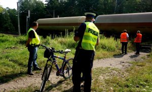 Policjant, pracownik PLK oraz funkcjonariusz SOK rozmawiają z rowerzystą, w tle widać jadący pociąg.
