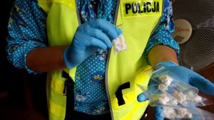 Nieumundurowana policjantka w żółtej kamizelce trzyma w rekach woreczki strunowe z zawartością amfetaminy.