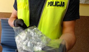Policjant w odblaskowej kamizelce z napisem &quot;Policja&quot; trzyma worek strunowy, w którym pozawijana jest w folię aluminiową amfetamina.