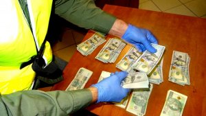 Nieumundurowany policjant w żółtej kamizelce i rękawiczkach liczy pieniądze i rozkłada je na biurku.