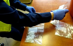 Policjant w kamizelce odblaskowej i rękawiczkach układa na biurku woreczki z amfetaminą.
