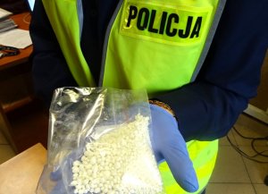 Policjant w kamizelce odblaskowej i rękawiczkach trzyma w rekach woreczek strunowy z amfetaminą.