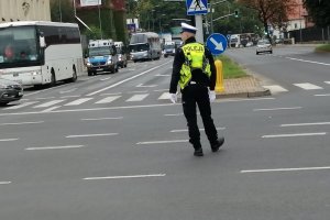 Policjant z ruchu drogowego w żółtej kamizelce na skrzyżowania kieruje ruchem.