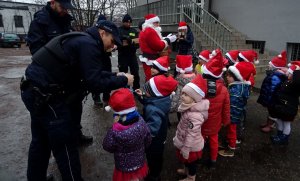 Na zdjęciu widoczne dzieci w czerwonych czapeczkach, policjanci, mikołaj, a także funkcjonariusze Straży Miejskiej.