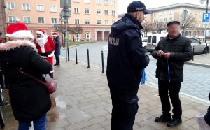 Policjant rozmawia z mężczyzną, dalej widoczne inne osoby Mikołaj.
