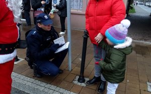 Policjant trzyma kolorowanki, kuca i rozmawia z dzieckiem,