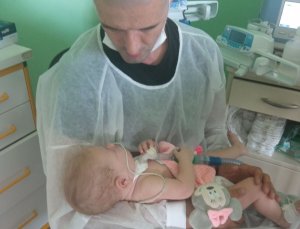 Mężczyzna trzyma na rękach córkę, która przypięta jest do respiratora, znajdują się w szpitalu.