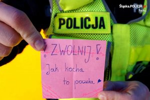 Policjant trzyma kartkę na której jest napisane &quot;Zwolnij, jak kocha to poczeka&quot;