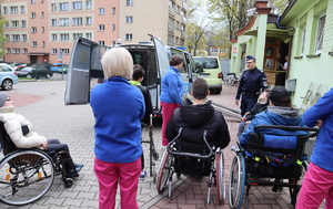 Na zdjęciu widoczne osoby na wózkach inwalidzkich, ich opiekunowie, umundurowany policjant, radiowóz.