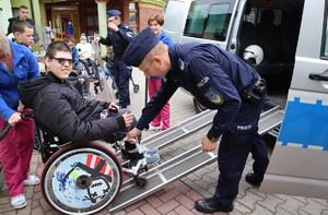 Policjant pomaga opuścić radiowóz osobie na wózku.