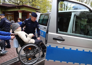 Policjant pomaga wjechać dziewczynie na wózku do policyjnego radiowozu.