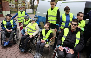 Zdjęcie grupowe, na którym widać opiekunów ośrodka oraz osoby niepełnosprawne na wózku, wszyscy w założonych odblaskowych kamizelkach.