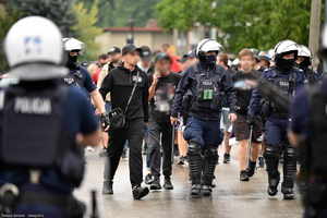 Policjanci zabezpieczający mecz prowadza na stadion grupę kibiców.