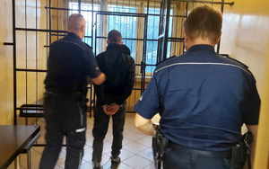 Policjanci doprowadzają zatrzymanego do tymczasowego pomieszczenia dla osób zatrzymanych.