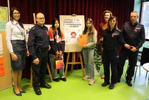 Zdjęcie grupowe policjantów, z dyrektorką szkoły oraz jej zastępcą, a także dwiema uczennicami, które wygrały konkurs na pracę plastyczną.