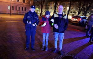 Na zdjęciu umundurowana policjantka z dwoma mężczyznami. Policjantka trzyma w rękach opaski odblaskowe.