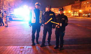 Na zdjęciu policjanci w mundurach oraz funkcjonariusz straży pożarnej. Funkcjonariusze trzymają w rękach odblaski. Za nimi radiowóz.