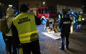 Na zdjęciu funkcjonaiusze policji, straży miejskiej oraz strażacy. Na środku zdjęcia fantom do udzielania pierwszej pomocy oraz klączący obok niego strażak i kobieta.