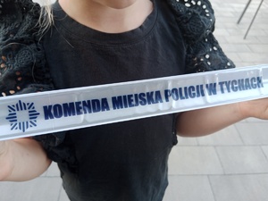 Na zdjęciu dziecko trzymające w rękach odblask z napisem Komenda Miejska Policji w Tychach.