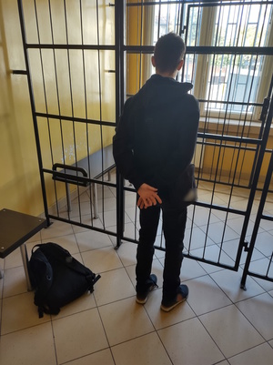 Na zdjęciu chłopak stojący w policyjnym pomieszczeniu do zatrzymań