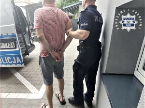 Na zdjęciu mężczyzna w kajdankach trzymany przez policjanta