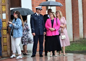 Na zdjęciu policjant oraz inne osoby przed wejściem do kościoła.