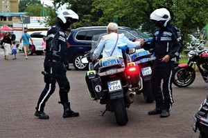 Na zdjęciu policjanci z Motocyklowej Asysty Honorowej pomagający kobiecie usiąść na motocyklu.