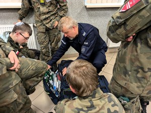 Na zdjęciu umundurowany policjant prezentujący uczniom wyposażenie torby medycznej.