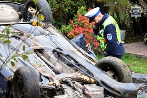 Na zdjęciu samochód uszkodzony w zdarzeniu drogowym. Obok niego umundurowany policjant.