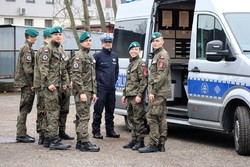 Na zdjęciu policjant ruchu drogowego oraz uczniowie klasy mundurowej stojący obok oznakowanego radiowozu.