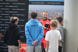 Kolorowe zdjęcie ratownika medycznego w towarzystwie młodzieży, który omawia zasady udzielania I pomocy.