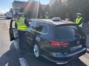 Kolorowe zdjęcie umundurowanych funkcjonariuszy policji oraz ITD przeprowadzających kontrolę pojazdu TAXI.