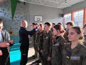 Kolorowe zdjęcie umundurowanego policjanta, który zakłada na szyję medal jednemu z uczestników konkursu.