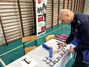 kolorowe zdjęcie umundurowanego policjanta rozkładającego na stole gadżety promujące Policję.