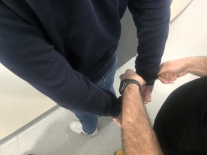 Kolorowe zdjęcie policjanta zakładającego kajdanki zatrzymanemu