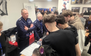 Grupa osób zainteresowana stoiskiem promocyjnym Policji. W tle widoczny umundurowany policjant.