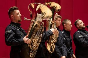 Policjanci orkiestry w mundurach policyjnych stojący z instrumentami na scenie.