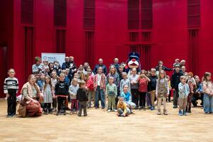 Sznupek w otoczeniu dzieci i policjantów stojących na scenie.