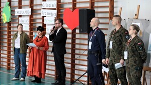 Oficjalne otwarcie eskulapiady. Przemawia dyrektor oraz organizatorka wydarzenia. Widoczni są również stojący obok przemawiających umundurowany policjant oraz kobieta i mężczyzna w mundurach wojskowych.