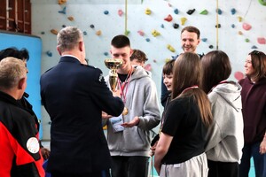 Komendant Komendy Miejskiej Policji w Tychach mł. insp. Tomasz Zawadzki wręczający uczniom puchar.