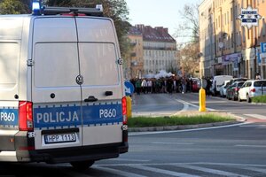 Tył oznakowanego radiowozu policyjnego w tle którego widać nadchodzących kibiców.